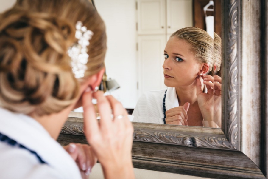 Photographie de la mariée mettant ses boucles d'oreilles devant son miroir